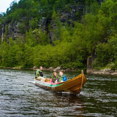 Et par i en liten motorbåt med båtfører på elv med fjell og grønt landskap rundt.