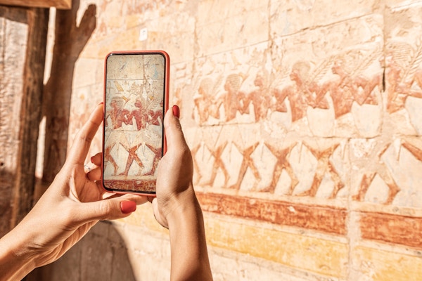 Reisebloggerjenta tar bilder på en smarttelefon ved de berømte freskene i Hatshepsut-tempelet i den gamle byen Luxor i Egypt. Eller ved hjelp av visuell turistguide
