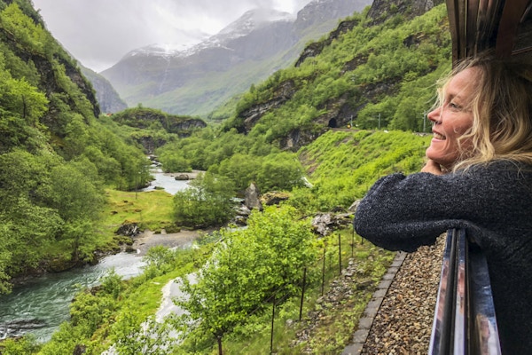 Dame ser ut av togvvindu på norsk fjellnatur.