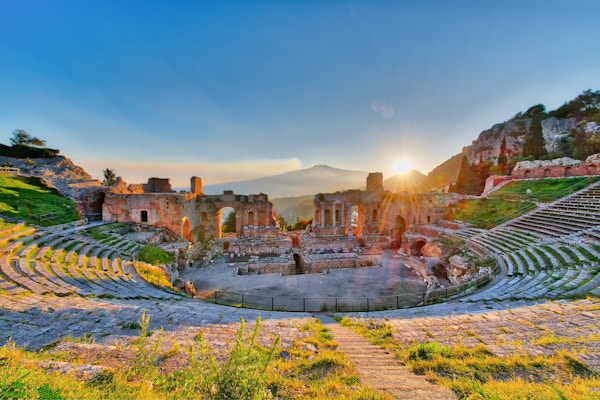 Det eldgamle teateret Taormina på Sicilia med Etna- vulkanens utbrudd i solnedgang