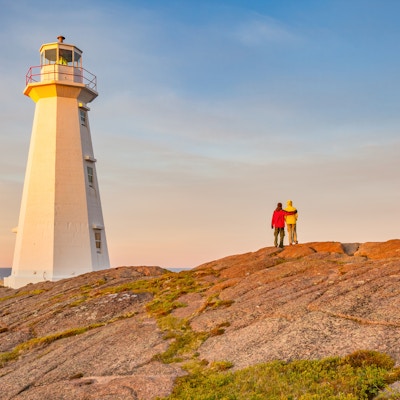 Arkivfotografi av par som omfavner ved landemerket Cape Spear Lighthouse nær St John's, Newfoundland, Canada ved solnedgang. Cape Spear er det østligste punktet i Canada.