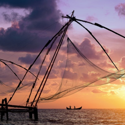 Vakker solnedgang over kinesiske fiskegarn og en båt i Kochi, Kerala, India