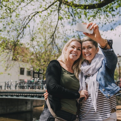 To kvinner i Amsterdam som tar en selfie ved elven.