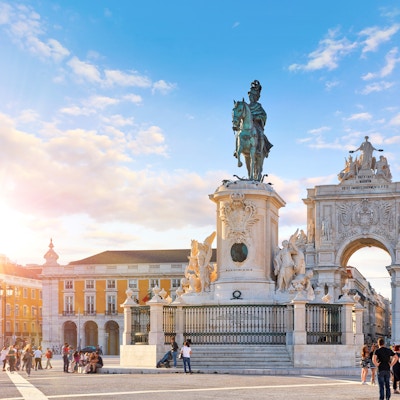 Lisboa, Portugal. Kong Jose I-statuen ved Praca do Comercio foran Triumfbuen nær vannkanten. Gamlebyen i Lisboa i det historiske sentrum av Alfama-distriktet. Kveldsolnedgang og blå himmel med skyer.