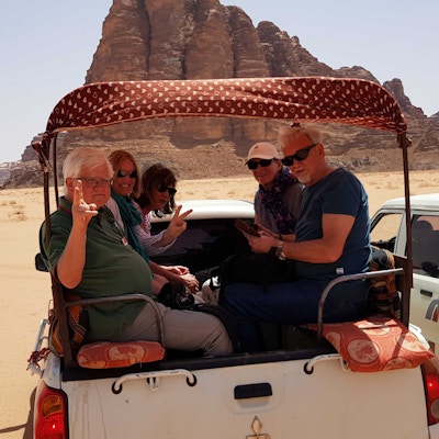 Gruppe med mennesker i jeep i ørken med fjell bak.