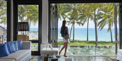 Hotellobby med dame som ser utover havet og stranda med palmer.