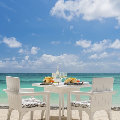Dekket bord for to på hvit strand med hav og himmel.