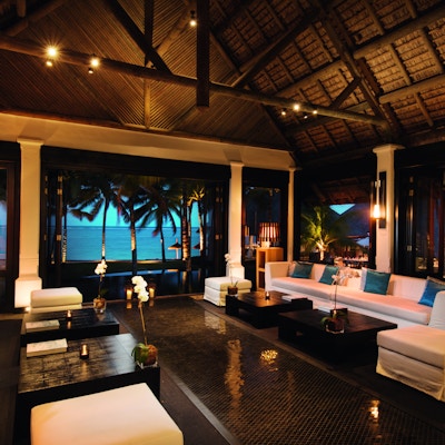 Elegant hotellobby med dempet belysning og hav og palmer utenfor.