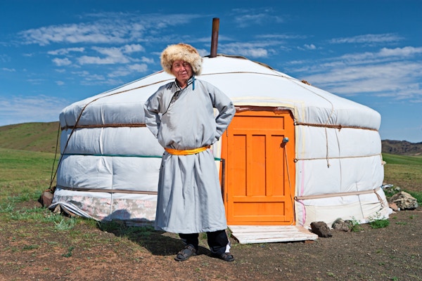 Mongolsk mann i nasjonale klær som står ved siden av ger (yurt). En yurt er en bærbar, filtdekket, trerammet innrammet boligstruktur som tradisjonelt brukes av nomader i steppene i Sentral-Asia. En yurt er mer hjemmelignende enn et telt i form og bygg, med tykkere vegger.