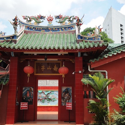 Rød inngangn til et tempel med grønt tak. Mange grønne planet, to kinesiske lykter, kinesike drager på toppen av inngangen.