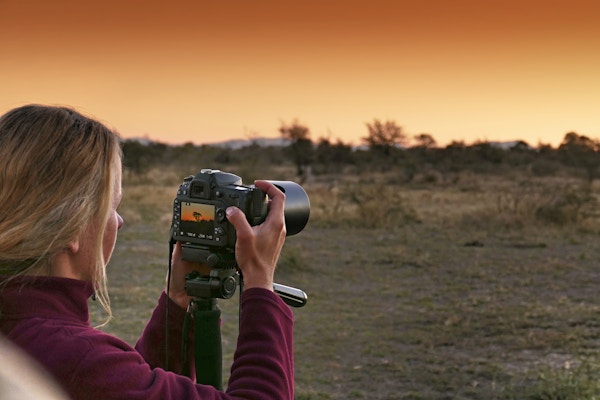 Turist tar bilder med et digitalt kamera montert på et stativ under en vakker solnedgang.