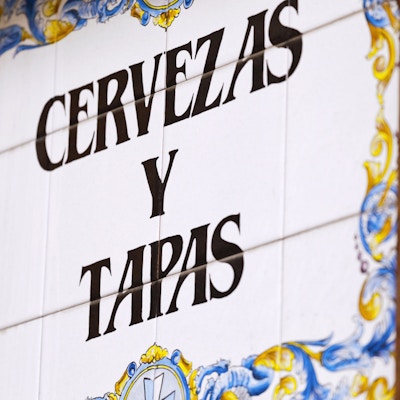 Gamle, spanske keramiske håndmalte fliser med et skilt som markedsfører øl og tapas snacks.