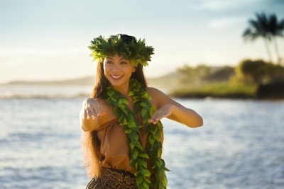 En vakker hawaiiansk huladanser som danser på stranden på de tropiske Hawaiiske øyene. Hun har på seg en tradisjonell Hula-dansekjole med en lei og hodepryd. Fotografert i vertikalt format med kopiplass i Kauai, Hawaii.