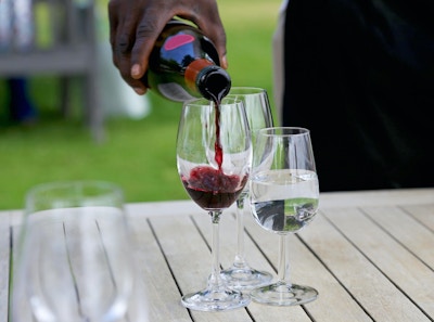 Servitør helle rødvin i et glass for vinsmaking, et glass vann også på bordet.
