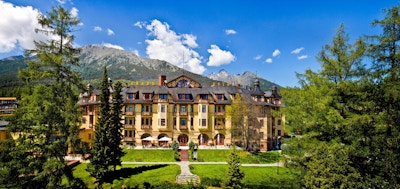 Fasade på hotell med hage i forkant og fjell i bakgrunnen