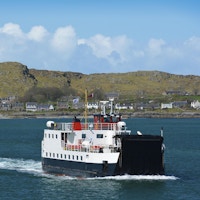 En ferge går tilbake fra Isle of Iona til Isle of Mull i Skottland over nydelig blått farvann.