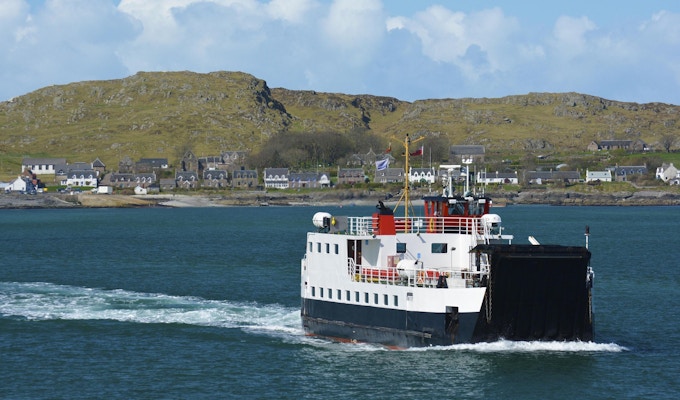 En ferge går tilbake fra Isle of Iona til Isle of Mull i Skottland over nydelig blått farvann.