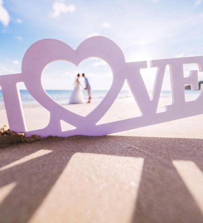 Skilt - "kjærlighet" på sandstranden med par inne i hjertet.