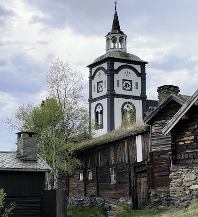 Kirketårn i svart og hvitt, med tradisjonelt gårdstun i forkant.