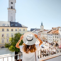 Ung kvinnelig turist som nyter en flott utsikt over den gamle bydelen med rådhustårnet i Lviv sentrum i det solfylte været i Ukraina
