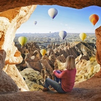 Kvinne som ser på fargerike luftballonger som flyr over dalen ved Cappadocia, Tyrkia. Vulkanske fjell i Goreme nasjonalpark.