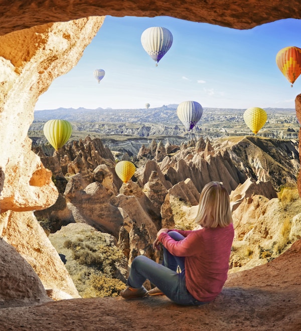 Kvinne som ser på fargerike luftballonger som flyr over dalen ved Cappadocia, Tyrkia. Vulkanske fjell i Goreme nasjonalpark.