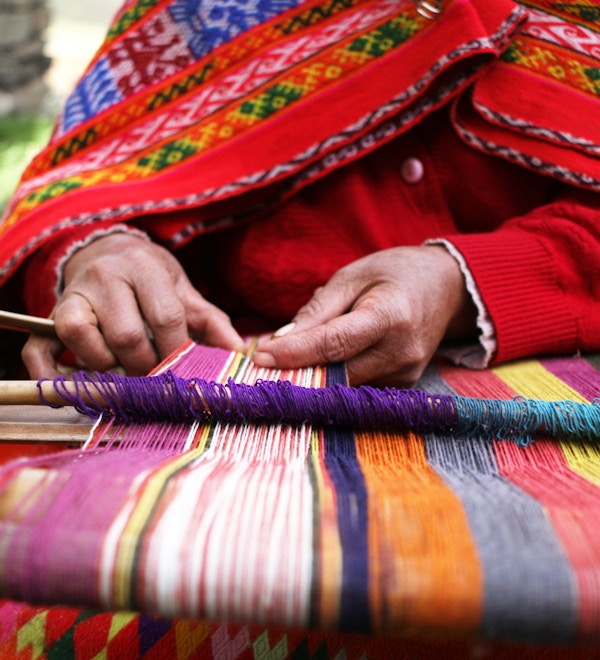 Et nærbilde av en kvinne som vever i Peru med lyse tradisjonelle klær.