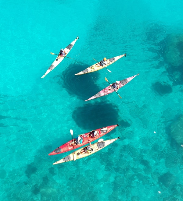 En gruppe padlere i fargerike kajakker på asurblått hav