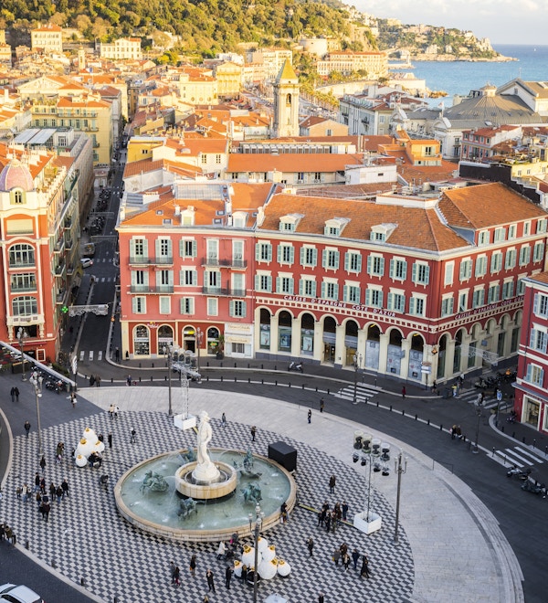 En luftfoto av Fontaine du Soleil på Place Messena, Nice. Med den nye trikkebanen og bygninger i Nice og havet i bakgrunnen.