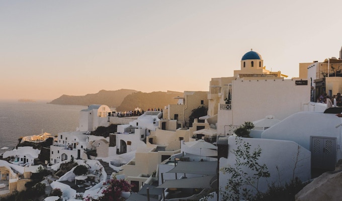 Utsikt over klassiske greske bygninger ved havet og en disig himmel i solnedgangsfarger