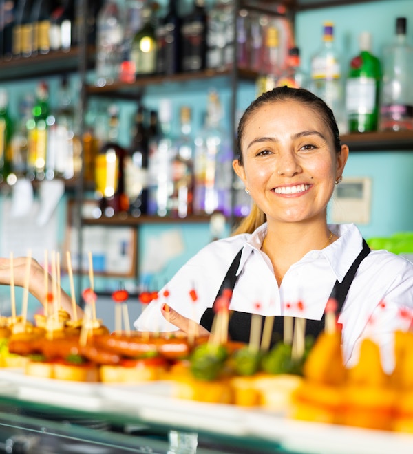 Blid latinsk kvinnelig bartender i uniform som serverer deilige tapas på spyd ved disken i baren