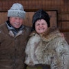 En mann og ei dame ikledd vinterklær og pels ønsker velkommen til fjells foran ei tredør