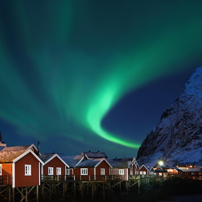 Nydelig form på nordlys (Aurora borealis) over tradisjonelle norske fiskehytter (rorbuer) og snøhvit fjell.