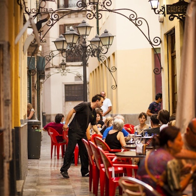 "Malaga, Spania - 8. august 2011: Folk sitter på atmosfæriske fortauskafeer i det historiske distriktet Malaga i Sør-Spania sent på ettermiddagen. En servitør kan sees som serverer drikke."
