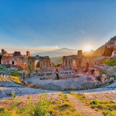 Det eldgamle teateret Taormina på Sicilia med Etna- vulkanens utbrudd i solnedgang