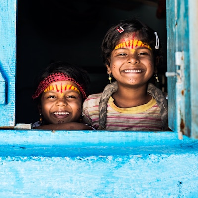 To små indiske søstre smiler på vinduet til det blå huset deres.