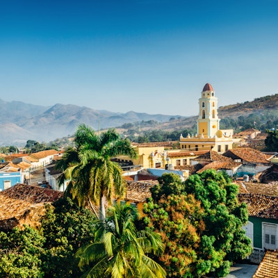 Panoramautsikt over byen Trinidad, Cuba, med fjell i bakgrunnen og en blå himmel. Klokketårnet tilhører Iglesia y Convento de San Francisco.