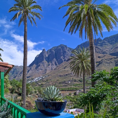 Naturen på Gran Canaria med fjell, palmer og blå himmel samt en blå krukke med agave i