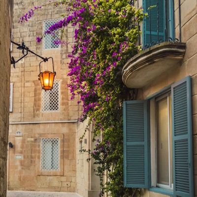 Mdina, Malta: tradisjonelt maltesisk hus med kunstnerisk balkong og vinduer, dekket med lyse lilla blomster på kalksteinsveggen og lanternelys