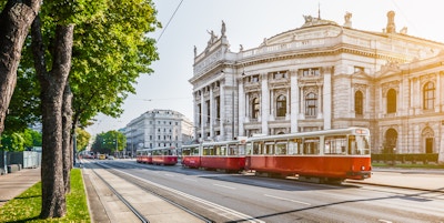 Den berømte Wiener Ringstrasse med det historiske Burgteateret (Imperial Court Theatre) og en tradisjonell rød, elektrisk trikk i soloppgang sett med retro vintage filtereffekt i Wien, Østerrike.