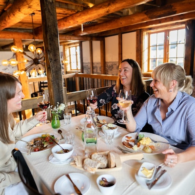 Tre damer med mat og drikke rundt restaurantbord.