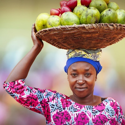 Portrett av rwandisk kvinne som bærer på hodet flettet kurv full av frukt