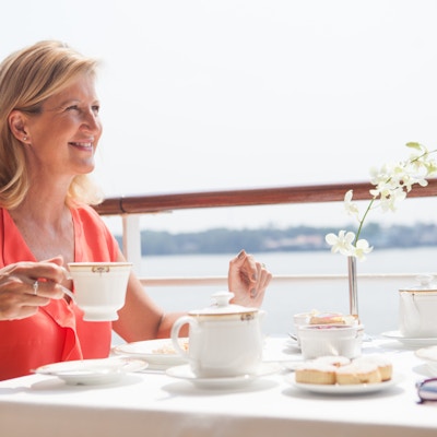 Kvinne drikker kaffe ved frokostbordet på skipsdekk.