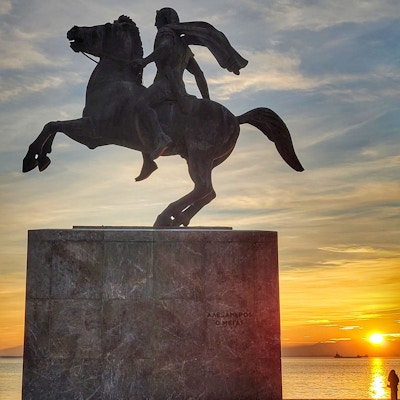 En statue av en mann på hest ved havet i solnedgang