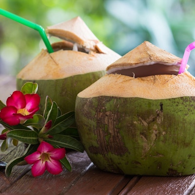 To kokosnøtter med sugerør pyntet med rosa blomster ved siden av